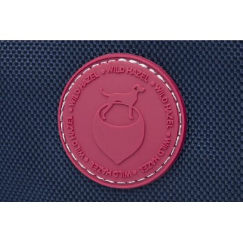 Ein kastanienbraunes, rundes Logo mit einem Hund, der auf einer Eichel steht, umgeben von dem Text "WILD HAZEL", der am Rand wiederholt wird.