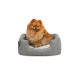Ein flauschiger orangefarbener Pomeranian-Hund sitzt bequem in einem grauen Haustierbett mit einem weichen weißen Innenraum und lächelt in die Kamera.