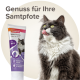 Eine flauschige graue Katze mit gelben Augen leckt sich die Lippen neben einer Tube Beaphar Malt Paste, beschriftet mit "Genuss für Ihre Samtpfote" und "mit MOS."