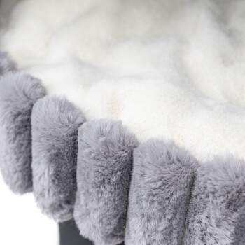 Eine Nahaufnahme eines weichen, plüschigen Haustierbettes mit einem weißen, flauschigen Innenraum und einem grauen Fellrand an den Kanten.