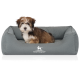 Ein kleiner, flauschiger Hund sitzt bequem in einem grauen Haustierbett, mit dem Logo "KNUFFELWUFF" sichtbar auf der Vorderseite.