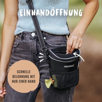 Eine Person in einem hellblauen Oberteil und schwarzen Jeans greift in eine "RUDELKÖNIG"-Leckerlitasche für schnelle Belohnungen.
