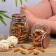 Zwei Glasbehälter gefüllt mit Haustierleckereien, einer umgekippt und verstreut Leckereien auf einem Holztisch, mit einem rosa Sofa und Seilspielzeugen im Hintergrund.