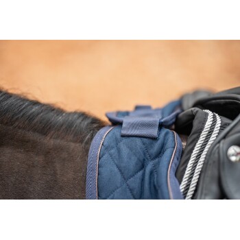 Nahaufnahme eines marineblauen, gesteppten Sattels, der auf dem Rücken eines Pferdes liegt, mit Fokus auf den Riemen und Nähdetails.