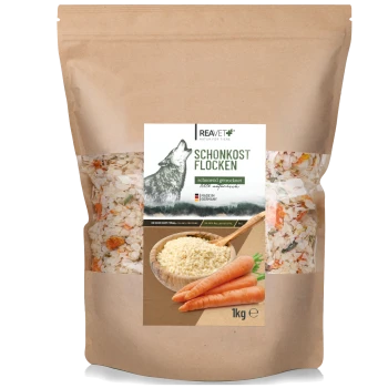 Eine 1-kg-Tüte REAVET-Hundefutter mit einem Wolf-Motiv, beschriftet mit "SCHONKOST FLOCKEN", mit einer Schüssel Futter und Karotten auf der Vorderseite.