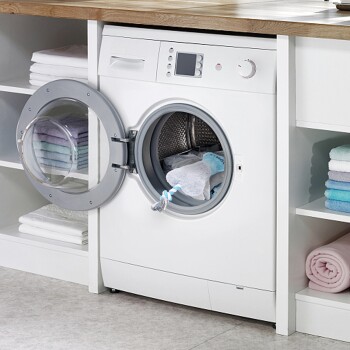 Eine Frontlader-Waschmaschine mit offener Tür, die ein blaues und weißes Hundespielzeug im Inneren zeigt, umgeben von ordentlich gestapelten Handtüchern.