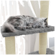 Eine flauschige graue Katze schläft friedlich auf einem weichen, grauen Regal eines Katzenbaums, mit einem sisalumwickelten Pfosten daneben und durchsichtigen Vorhängen im Hintergrund.