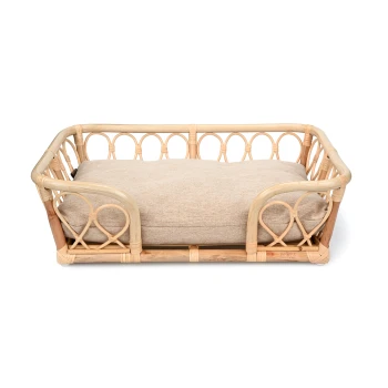 Rattan Korb Bali L-XL Ein stilvolles Haustierbett aus natürlichem Rattan mit einem weichen beigen Kissen, das ein dekoratives, geschwungenes Design und offene Seiten aufweist.