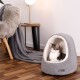 Ein graues Katzenbett mit weißem Innenraum hält eine getigerte Katze. Eine weiche graue Decke liegt in der Nähe, mit einer modernen Lampe im Hintergrund.