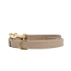 Eine beige Leder-Hundeleine mit einem goldenen Metallclip und D-Ring, ordentlich auf einem weißen Hintergrund gewickelt.
