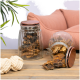 Zwei Glasbehälter gefüllt mit Haustierleckerlis, einer umgekippt und verschüttet Leckerlis, auf einem Holztisch neben einem Seilspielzeug und einem rosa Haustierbett.