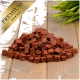 Ein Haufen kleiner, quadratischer, rötlich-brauner Haustierleckerlis auf einer Holzoberfläche, mit einem goldenen 'PREMIUM'-Label in der oberen linken Ecke.