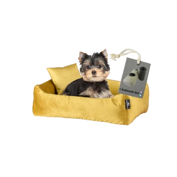 Ein kleiner Yorkshire Terrier Welpe sitzt auf einem plüschigen gelben Hundebett mit einem passenden Kissen, mit einem Etikett, das '+ Kotbeutel Set' liest.