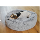Kleiner dreifarbiger Hund ruht mit dem Kopf am Rand eines runden, flauschigen grauen Hundebetts auf einem Holzboden.