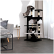 Ein stilvoller Katzenbaum in Schwarz und Weiß mit zwei Katzen, die darin entspannen, eine Katze klettert hinunter, in einem modernen Wohnzimmer mit einem grauen Sofa und einem kleinen Tisch.