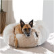 Ein entspannter Hund mit braunem und schwarzem Fell ruht auf einem flauschigen, cremefarbenen Haustierbett, mit einem schwarzen Etikett, das an der Seite sichtbar ist.