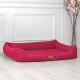 Ein stilvolles rotes Hundebett mit weißem Piping und einem kleinen braunen Etikett, auf einem hellen Holzboden vor einer weißen Wand platziert.