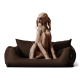 Ein hellbrauner Hund, der auf einem plüschigen, dunkelbraunen Hundebett mit zwei Seitkissen aufrecht sitzt und aufmerksam zur Seite schaut.