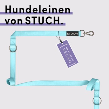 Eine hellblaue Hundeleine von STUCH, mit einem schwarzen Etikett mit dem Markennamen und einem Anhänger, der "PETA APPROVED VEGAN" liest.