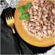 Une assiette dorée de nourriture humide pour animaux en morceaux avec une sauce crémeuse, des herbes et une fourchette dorée sur une serviette sombre.