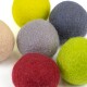 Eine Sammlung von sechs bunten Filzkugeln in verschiedenen Farbtönen, darunter rot, grau, grün, gelb, beige und dunkelblau, eng beieinander angeordnet.