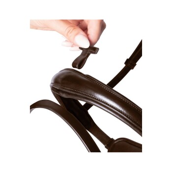 Eine Hand hält einen kleinen braunen Clip, der an ein braunes Leder-Hundegeschirr befestigt ist, und zeigt das Design und Material des Geschirrs.