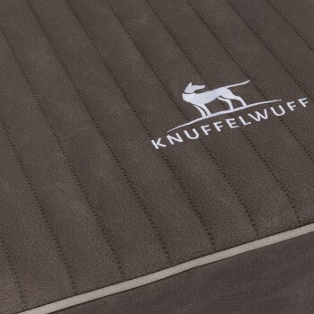 Eine Nahaufnahme eines braunen Haustierbettes mit vertikaler Naht und dem gestickten Logo 'KNUFFELWUFF' mit einer Silhouette eines Hundes.