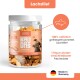 Eine Hand hält einen Hundesnack mit der Aufschrift "100% Lachs", "0g", "Ohne Zucker oder Zusatzstoffe" und "Ideal für Training & Belohnung."
