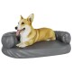 Ein entspannter Corgi liegt auf einem grauen Hundebett mit erhöhten Seiten und zeigt seinen verspielten Ausdruck mit herausgestreckter Zunge.