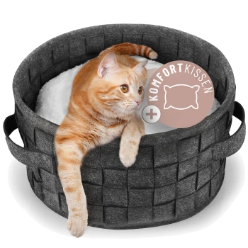 Orange getigerte Katze liegt in einem dunkelgrauen, gewebten Haustierbett mit weißem Kissen, beschriftet mit "Komfort Kissen".