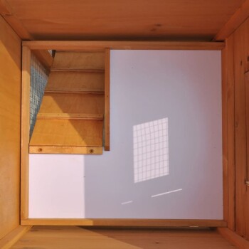 Innenansicht eines hölzernen Haustierhauses mit einer Treppe, die nach oben führt, mit Sonnenlicht, das einen Gitter-Schatten an die Wand wirft.