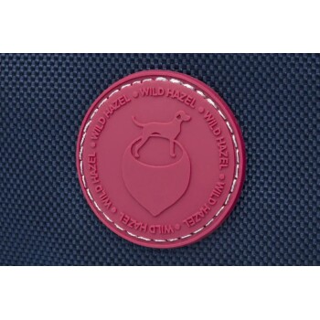 Ein rundes, kastanienbraunes Gummipatch mit der Silhouette eines Hundes über einer Herzform, umgeben von dem Text 'WILD HAZEL', der am Rand wiederholt wird.