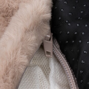 Nahaufnahme einer Haustiertrage mit weichem beigen Kunstfellfutter, einer schwarzen strukturierten Außenseite und einem Reißverschlussdetail.