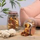 Zwei Glasbehälter mit Haustierleckereien, einer umgekippt und verschüttet Leckereien auf einem Holztisch, mit einem rosa Sofa und einer grünen Pflanze im Hintergrund.