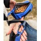 Eine Person hält eine blaue Leckerlitasche für Haustiere, gefüllt mit kleinen, rechteckigen Leckerlis, und einem blauen Karabiner, der an der Tasche befestigt ist.