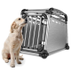 Golden-Retriever-Welpe sitzt neben einer silbernen Aluminium-Transportbox für Hunde mit Rohrrahmen und Netzwänden.
