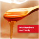 Goldener Honig, der von einem Holzlöffel tropft, rotes Etikett mit der Aufschrift 'Mit Vitaminen und Honig'.