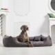 Ein brauner Hund liegt auf einem plüschigen grauen Hundebett in einem stilvollen Raum mit weißen Wänden und dekorativen Elementen.