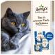 Eine graue Katze mit gelben Augen ruht neben einer Anzeige für Betty's Landhausküche Katzenfutter, die Fischgeschmäcker bewirbt.