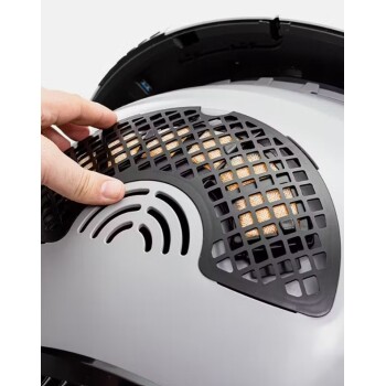 Eine Person hält eine schwarze, gittermusterartige Abdeckung eines Haustierprodukts, die eine strukturierte Oberfläche darunter zeigt, wahrscheinlich einen Filter.