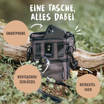 Eine schwarze multifunktionale Tasche auf einem Baumstamm im Gras, mit Fächern für ein Handy, Schlüssel und einen Müllbeutel. Text: "EINE TASCHE, ALLES DABEI."