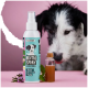 Eine türkisfarbene und rosa "DENTALSPRAY"-Flasche, ein Glasgefäß, ein Minzzweig und ein neugieriger schwarz-weißer Hund im Hintergrund.