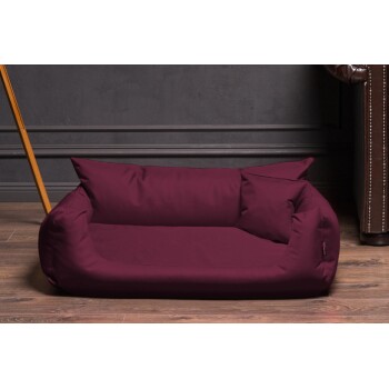 Burgunderfarbener Haustierbett mit zwei seitlichen Kissen, auf Holzboden vor einer dunklen Wand platziert, ideal für kleine bis mittelgroße Haustiere.