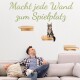 Mann sitzt auf der Couch und schaut auf eine Katze auf hölzernen Wandregalen, darüber deutscher Text "Macht jede Wand zum Spielplatz".
