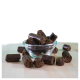 Eine klare Glasschüssel gefüllt mit kleinen, dunkelbraunen Haustierfutterpellets, umgeben von verstreuten Pellets auf einer Holzoberfläche.