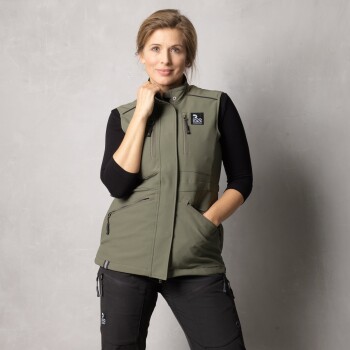 Ein Modell, das eine grüne ärmellose Weste mit einem Logo trägt, kombiniert mit schwarzen Hosen, posiert vor einem neutralen Hintergrund.