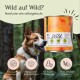 Ein glücklicher Hund im Wald schaut auf eine Dose "Wild" Haustierfutter mit Amaranth, Brokkoli und Leinsamenöl, gekennzeichnet mit "Monoprotein" und "Getreidefrei."