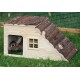 Ein brauner Hase schaut aus einem Holzhaustierhaus mit einem mit Rinde bedeckten Dach, das auf grünem Gras steht.