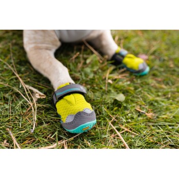 Nahaufnahme einer Hundepfote, die einen leuchtend gelben und grauen Hundestiefel auf Gras trägt, der sein schützendes Design zeigt.