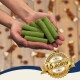 Hände halten grüne Kausticks, unscharfer Holzboden mit verstreuten Leckerlis und ein goldenes Abzeichen mit der Aufschrift '15 Jahren'.